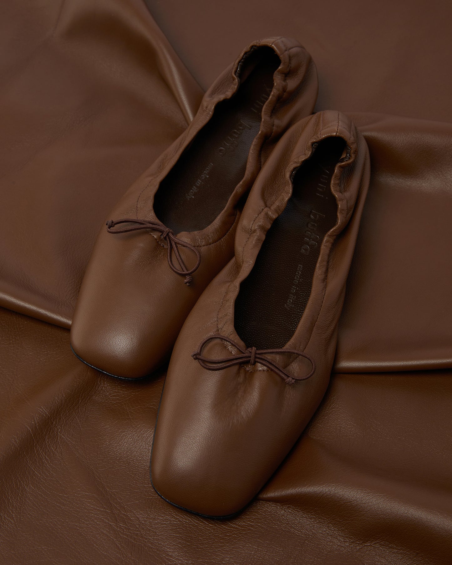 Close-up of Pia Ballerina Saddle Brown flats on leather fabric