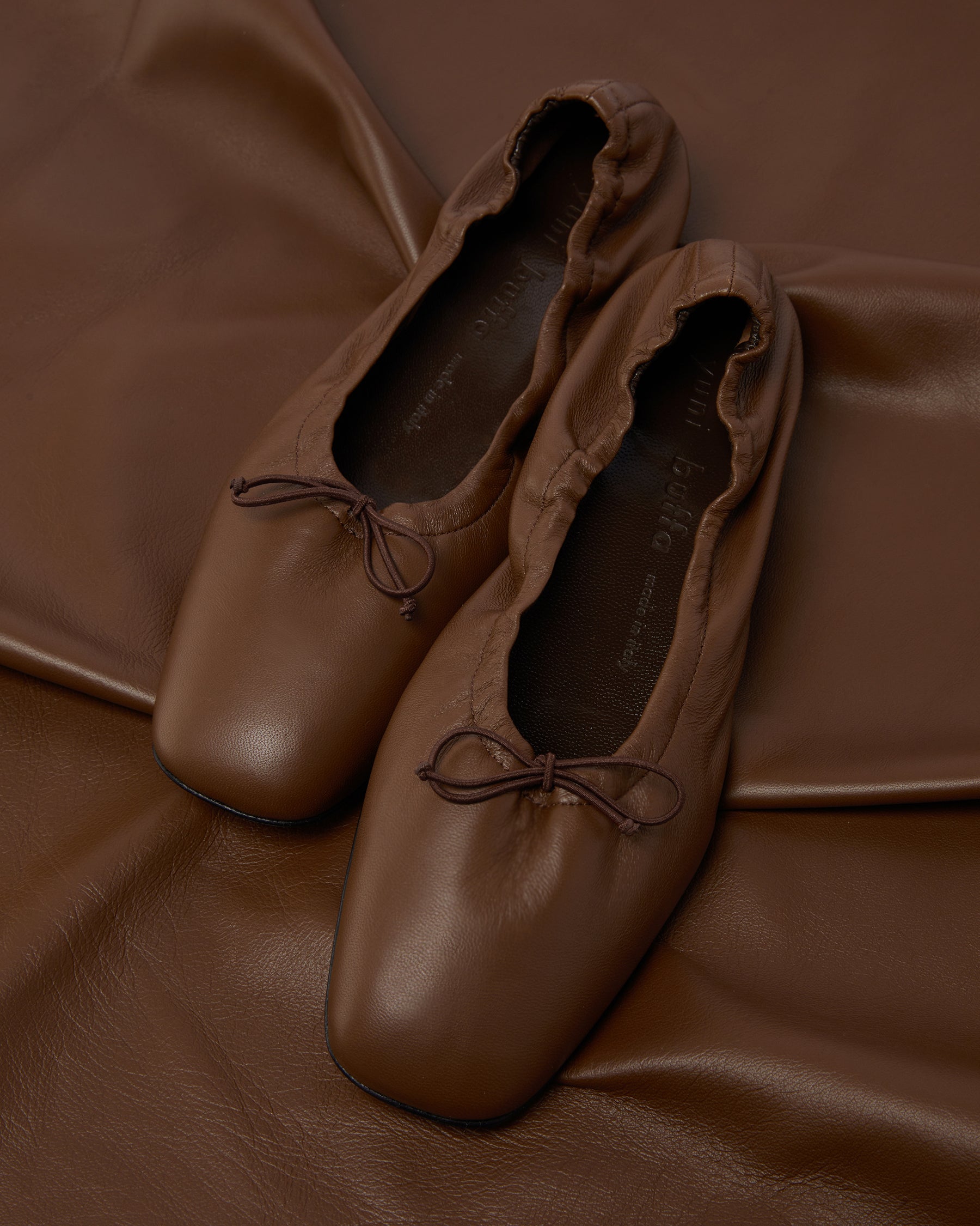 Close-up of Pia Ballerina Saddle Brown flats on leather fabric