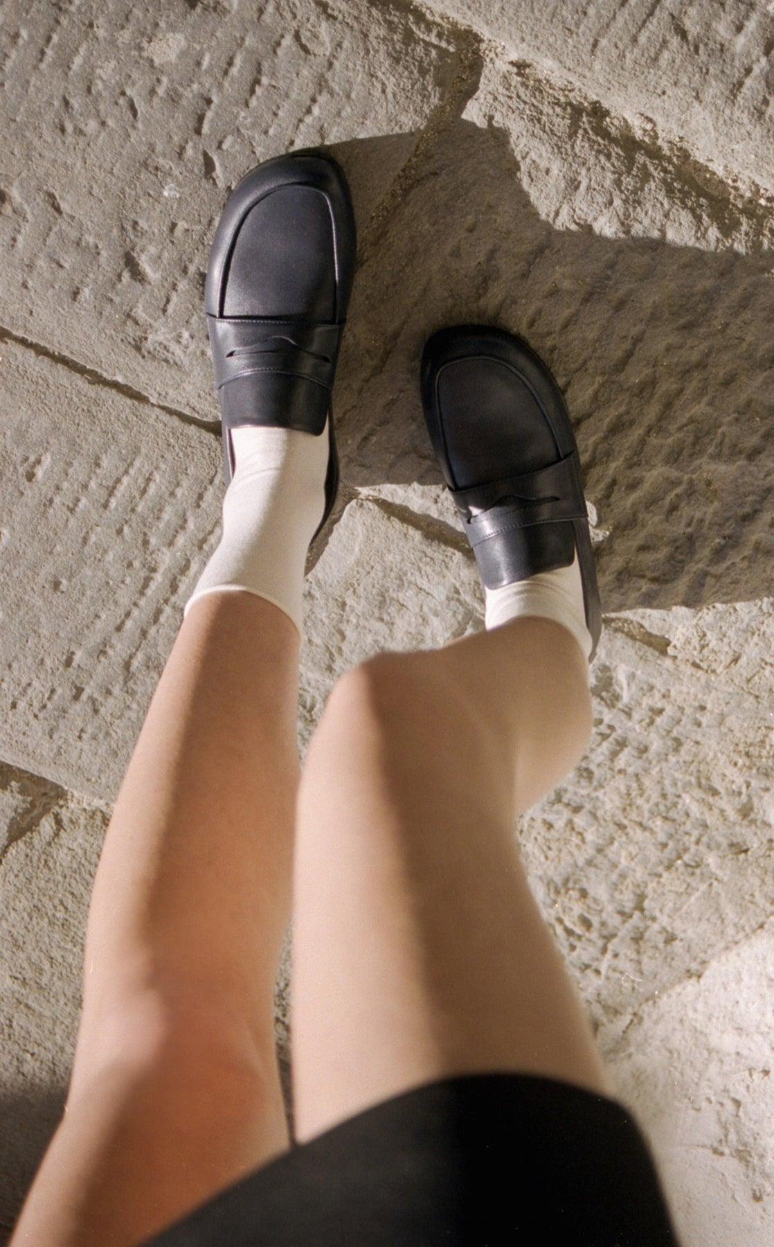 A model wearing navy loafers, styled with a classic outfit in a relaxed setting