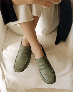 A model wearing Yuni Buffa Fez Penny Loafer shoes in Sage Green. Artisanal crafted women designer loafer shoe made in Italy with Italian Lamb Nappa leather.