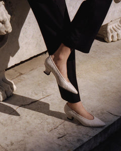 A model leaning on a wall wearing Yuni Buffa Roma Pump shoes in Cloud White. Handcrafted comfortable designer high-heels made  in Italy with Italian Lamb Nappa leather