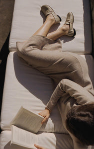 A model laying on a couch reading wearing Yuni Buffa Fez Penny Loafer shoes in Ecru beige.  Artisanal crafted women designer loafer shoe made in Italy with Italian Lamb Nappa leather.