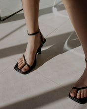 Load image into Gallery viewer, A model wearing Yuni Buffa Castrise strappy sandal Heel in Black color handmade in Italy with Italian Lamb Nappa leather and silver logo buckle in Tuscany, Italy