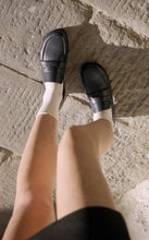 Load image into Gallery viewer, A model on the street wearing Yuni Buffa Fez Penny Loafer shoes in Navy with white socks.  Artisanal crafted women designer loafer shoe made in Italy with Italian Lamb Nappa leather.