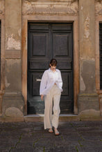 Load image into Gallery viewer, A model dressed in white walking away from a green door in a sunny tuscan town wearing Yuni Buffa Lucca Sardinian cork wedge sandal shoe in Ecru white color with tan vachetta leather insole and crepe rubber outsole made in Italy with Italian Lamb Nappa leather