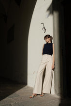 Load image into Gallery viewer, A model leaning on the wall wearing cashmere vest and white denim in a sunny tuscan town wearing Yuni Buffa Lucca Sardinian cork wedge sandal shoe in Ecru white color with tan vachetta leather insole and crepe rubber outsole made in Italy with Italian Lamb Nappa leather