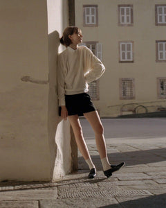 A model leaning on the wall in the sun in white sweater and black skirt wearing Yuni Buffa Fez Penny Loafer shoe in Navy blue color made in Italy with Italian Lamb Nappa leather