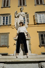 Load image into Gallery viewer, A model leaning on the water fountain in a Tuscan town wearing Yuni Buffa Roma Pump shoe in Cloud white color made in Italy with soft quilted Italian Lamb Nappa leather
