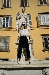 A model leaning on the water fountain in a Tuscan town wearing Yuni Buffa Roma Pump shoe in Cloud white color made in Italy with soft quilted Italian Lamb Nappa leather