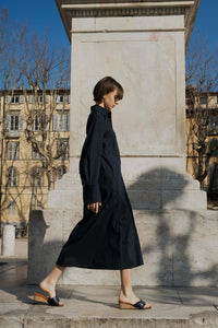 A model in a navy long shirt dress standing in a sunny Tuscan piazza wearing Yuni Buffa Lucca Sardinian cork wedge sandal shoe in Navy blue color with tan vachetta leather insole and crepe rubber outsole made in Italy with Italian Lamb Nappa leather