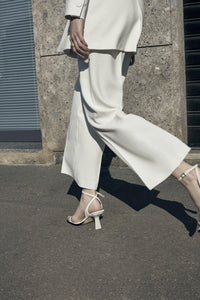 A model in white suit walking down the street in Milan wearing Yuni Buffa Castrise Heel in Cloud white color made in Italy with Italian Lamb Nappa leather and silver logo buckle