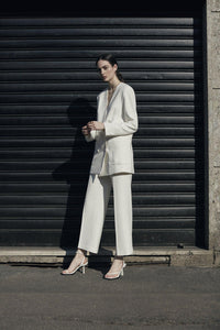 A model in white suit wearing Yuni Buffa Castrise Heel in Cloud white color made in Italy with Italian Lamb Nappa leather and silver logo buckle